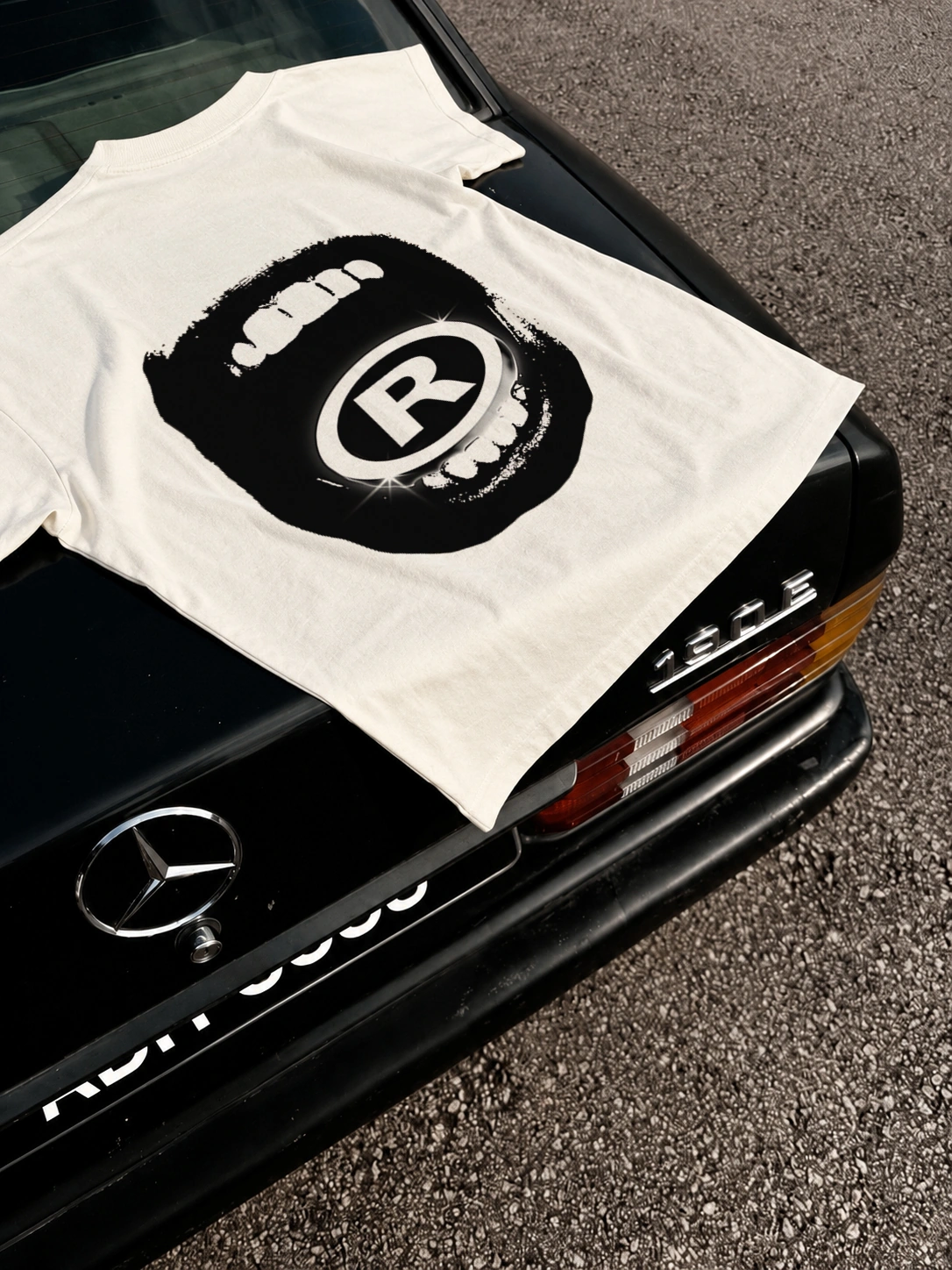 Camiseta Emoção off-white sobre a traseira de uma Mercedes, com a estampa original nas costas.