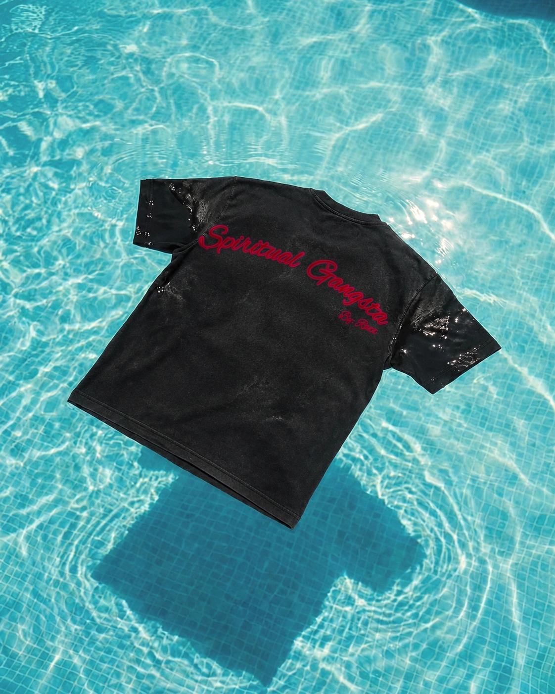 Spiritual Gangsta em preto marmorizado flutuando na piscina, com a inscrição vermelha original posicionada na parte superior das costas.
